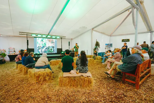Charla bajo la carpa, con el público sentado en fardos de paja